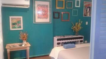 Une chambre avec des murs de couleur turquoise, un lit, une table de chevet avec un vase et des œuvres d’art encadrées.