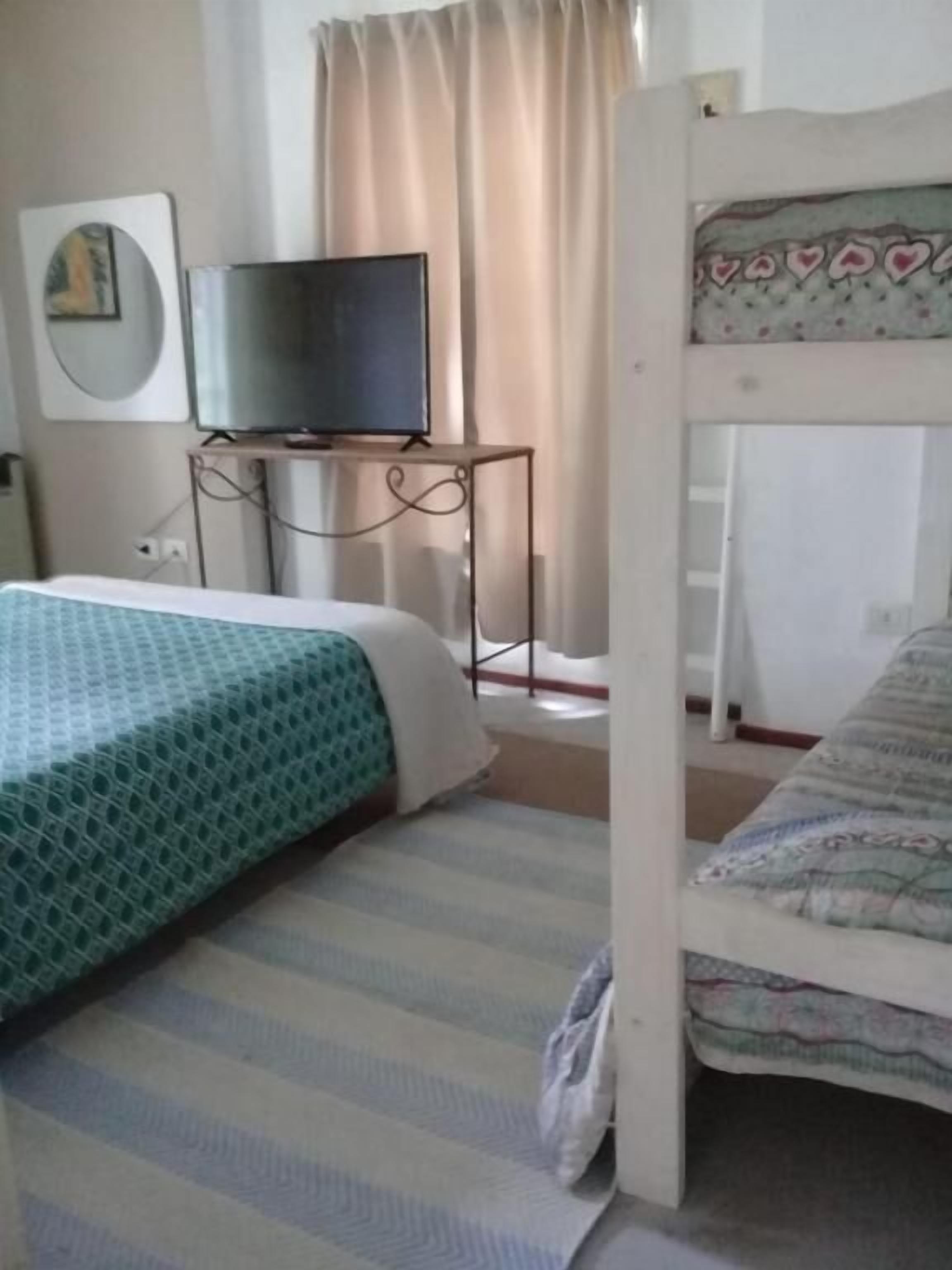 A bedroom with a bunk bed, a desk with a television, and a bed with a patterned bedspread.