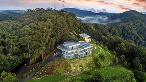 An aerial view of a modern, multi-story building surrounded by dense forest, with a clear path leading to the entrance. - ON TOP OF THE WORLD Garden Studio
Panoramic Ocean Views, Close to Town & Beaches (Korora)