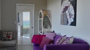 A living room with a purple sofa, a grey armchair, and a glass door leading to a balcony. - ON TOP OF THE WORLD Garden Studio
Panoramic Ocean Views, Close to Town & Beaches (Korora)