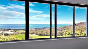 A room with large windows offering a view of a coastal landscape with hills and a body of water. - ON TOP OF THE WORLD Garden Studio
Panoramic Ocean Views, Close to Town & Beaches (Korora)