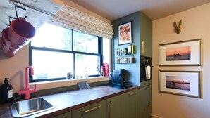 Una cocina con ventana, un lavamanos, armarios y una cafetera.
