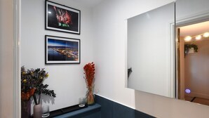 Un baño con espejo, dos fotografías enmarcadas en la pared, un jarrón con flores y un vaso sobre el mostrador.