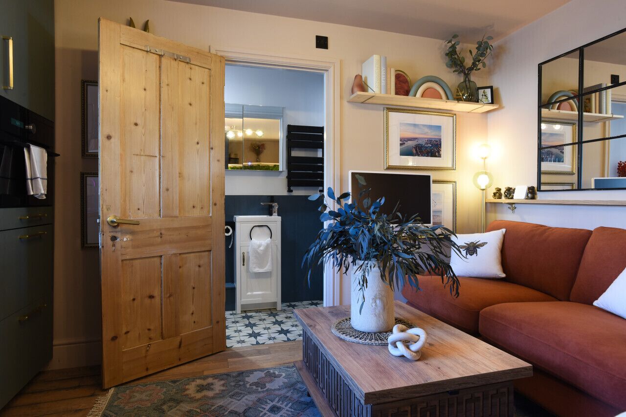 Un accogliente soggiorno con una porta in legno, un divano, un tavolino da caffè e una zona cucina visibile attraverso una porta aperta.
