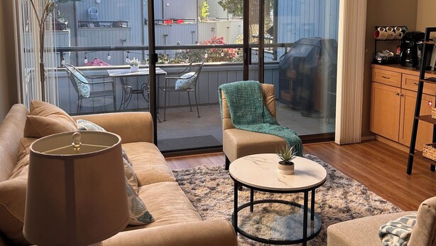 A spacious living room with a large sliding glass door leading to a balcony, a sofa, a coffee table, and a lamp.