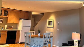 A spacious living area with a high ceiling, wooden flooring, a dining table with chairs, a sofa, and a lamp.