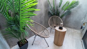 A small outdoor seating area with wicker chairs and a round wooden table, surrounded by large potted plants.