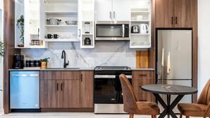 A modern kitchen with white cabinets, a built-in microwave, a stainless steel oven, and a black dishwasher. There is a round table with two chairs and a potted plant on the counter.