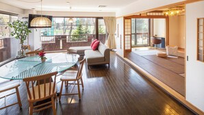 A modern living room with a glass-top dining table, wooden chairs, a sofa, and a tatami mat area. - Spacious 3-bedroom family-friendly parkside apartment w/WiFi in charming Sapporo (Sapporo)