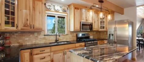 A kitchen with wooden cabinets, a granite countertop, stainless steel appliances, and a large window.