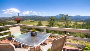 Eine Terrasse mit Glastisch und Stühlen, mit Blick auf eine malerische Landschaft mit Hügeln und Bäumen.
