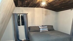 Ein Schlafzimmer mit einem Bett, einem Fenster mit Vorhängen, einer Chandelierleuchtre und Holzboden.