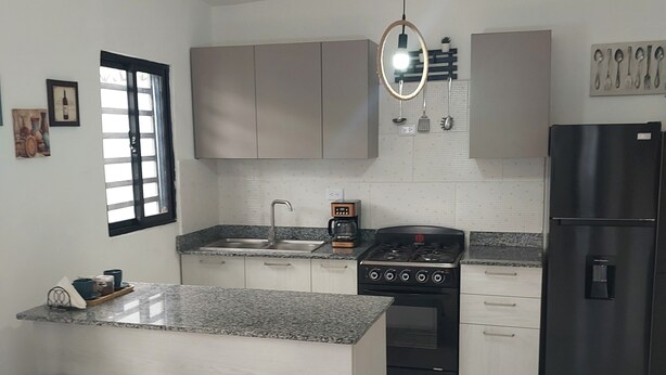Een moderne keuken met een centraal eiland, barkrukken, een fornuis, een koelkast en een raam met jaloezieën.
