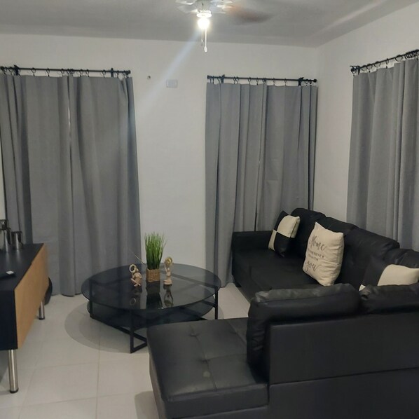 Un salón moderno con un sofá de cuero negro, una mesa de centro de vidrio y una mesita auxiliar.