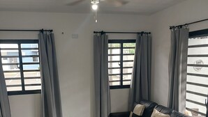 Een moderne woonkamer met een zwarte leren bank, een glazen salontafel en grijze gordijnen.