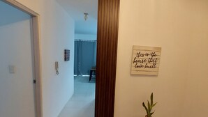 Een hal met een houten deur, een potplant en een bord aan de muur.