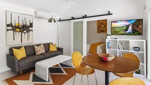 A modern living room with a sofa, coffee table, dining table, chairs, a TV, and artwork on the walls. - High Style Bohemian Zen Retreat, Saltwater Pool (Cathedral City)