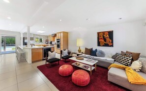 A modern living room with a sofa, ottomans, a coffee table, and a kitchen in the background.