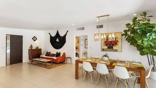 A modern living room with a dining area, a sofa, a coffee table, and a large plant. - High Style Bohemian Zen Retreat, Saltwater Pool (Cathedral City)