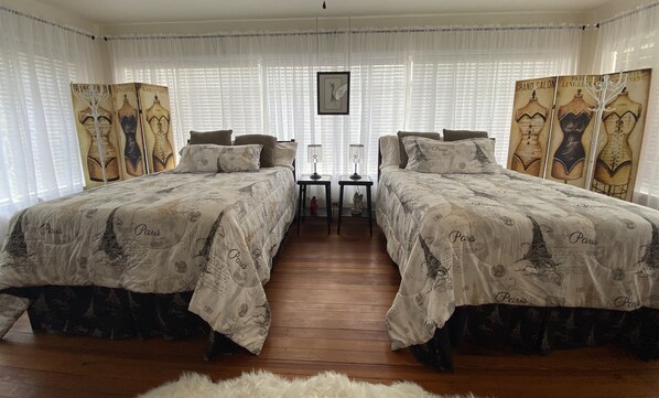 A room with two beds, each with a Paris-themed duvet cover, a small table with lamps, and a picture on the wall.