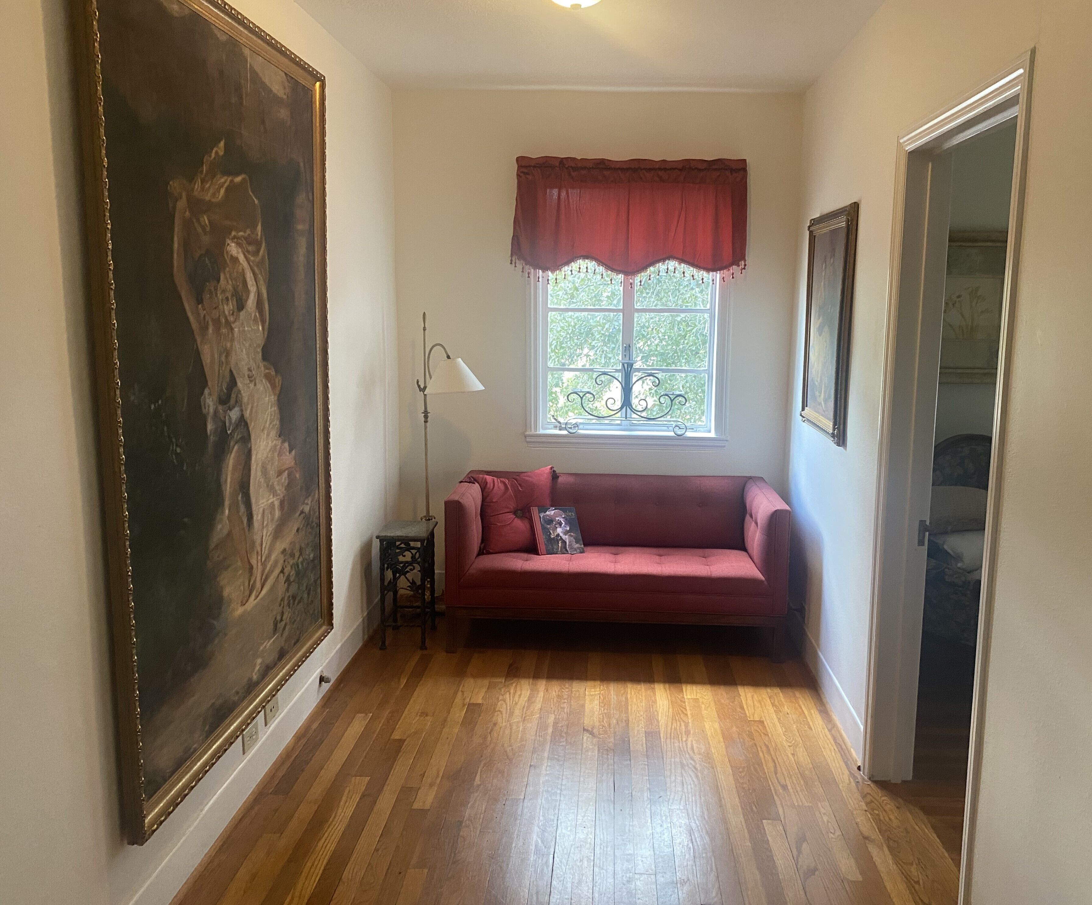 Habitació amb un sofà vermell, un quadre gran amb marc, una làmpada de peu i una finestra amb una cortina vermella.