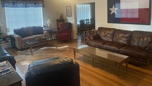 Ein Wohnzimmer mit einer Ledersofa, einem Glastisch und einem roten Sessel. Im Hintergrund steht ein Esstisch mit Stühlen.
