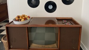 Ein altes Fernsehgerät mit Holzschrank, einer Obstschale und Schallplatten an der Wand.