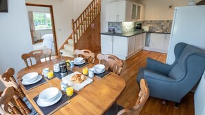 Un coin repas avec une table en bois mise pour le petit-déjeuner, un fauteuil bleu et une cuisine en arrière-plan.