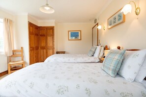 Une chambre avec deux lits, une armoire en bois, une chaise, une table de chevet et un tableau encadré au mur.