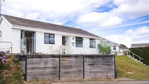 A white two-story house with a wooden fence, a dining area with chairs, and a staircase leading to the upper floor. - 113 Cae Du, Abersoch (Abersoch)
