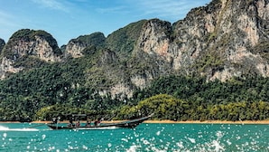 A boat on a turquoise sea with a mountainous backdrop. - Boom Hostel Khao Sok (Phanom)
