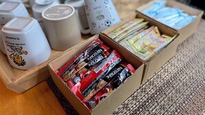 A table with various coffee products, including boxed coffee and coffee pods, and several ceramic mugs. - Boom Hostel Khao Sok (Phanom)