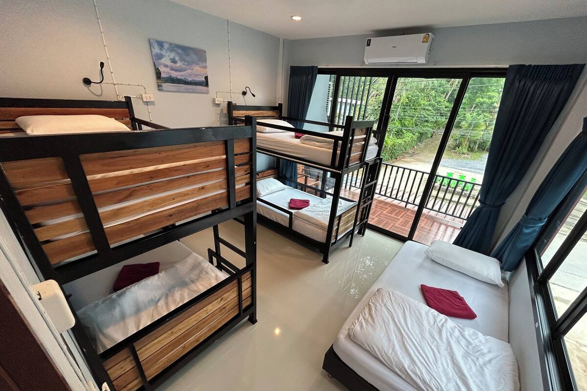 A dormitory room with bunk beds, a balcony with a view, and an air conditioning unit.