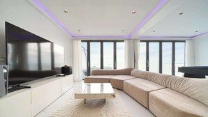 Ein modernes Wohnzimmer mit großem Flachbildfernseher, einem beigefarbenen Sofa, einem Couchtisch und einem gemusterten Teppich.