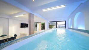 Ein Hallenbad mit weiter Aussicht, einem an der Wand befestigten Fernseher und einem Tisch mit Stühlen.
