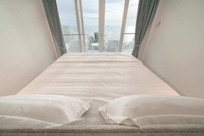 Un dormitorio con una cama grande, vistas al mar a través de ventanas de gran altura y un balcón con barandilla.