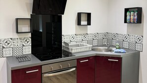 A modern kitchen with a black range hood, stainless steel appliances, and a patterned backsplash. - Appartement la Citadelle (Belfort)