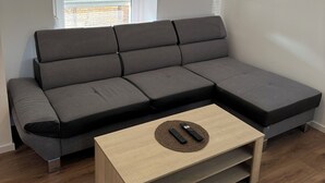 A modern living room with a sectional sofa, a wooden coffee table, and a ceiling light fixture. - Appartement la Citadelle (Belfort)