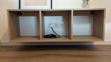 Una consola de madera con una fotografía enmarcada del paisaje urbano de París, un florero con flores secas y un adaptador de corriente con cable.