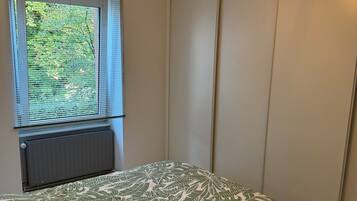 Una camera da letto con un letto, una finestra con persiane, un termosifone e una lampada a parete.