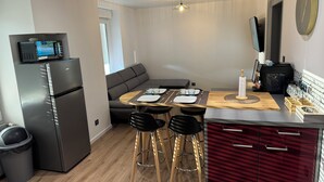 A modern kitchen with a refrigerator, microwave, and a dining area with a wooden table and bar stools. - Appartement la Citadelle (Belfort)