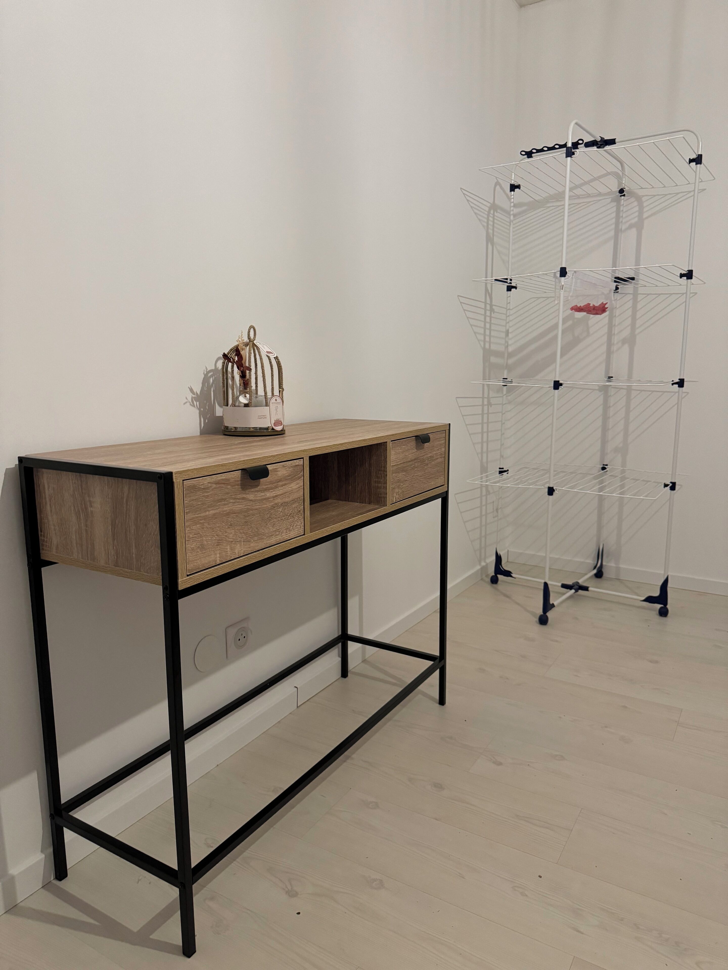 Een houten bureau met lades en een metalen frame, een wit draadrek en een pot met een plantje op het bureau.