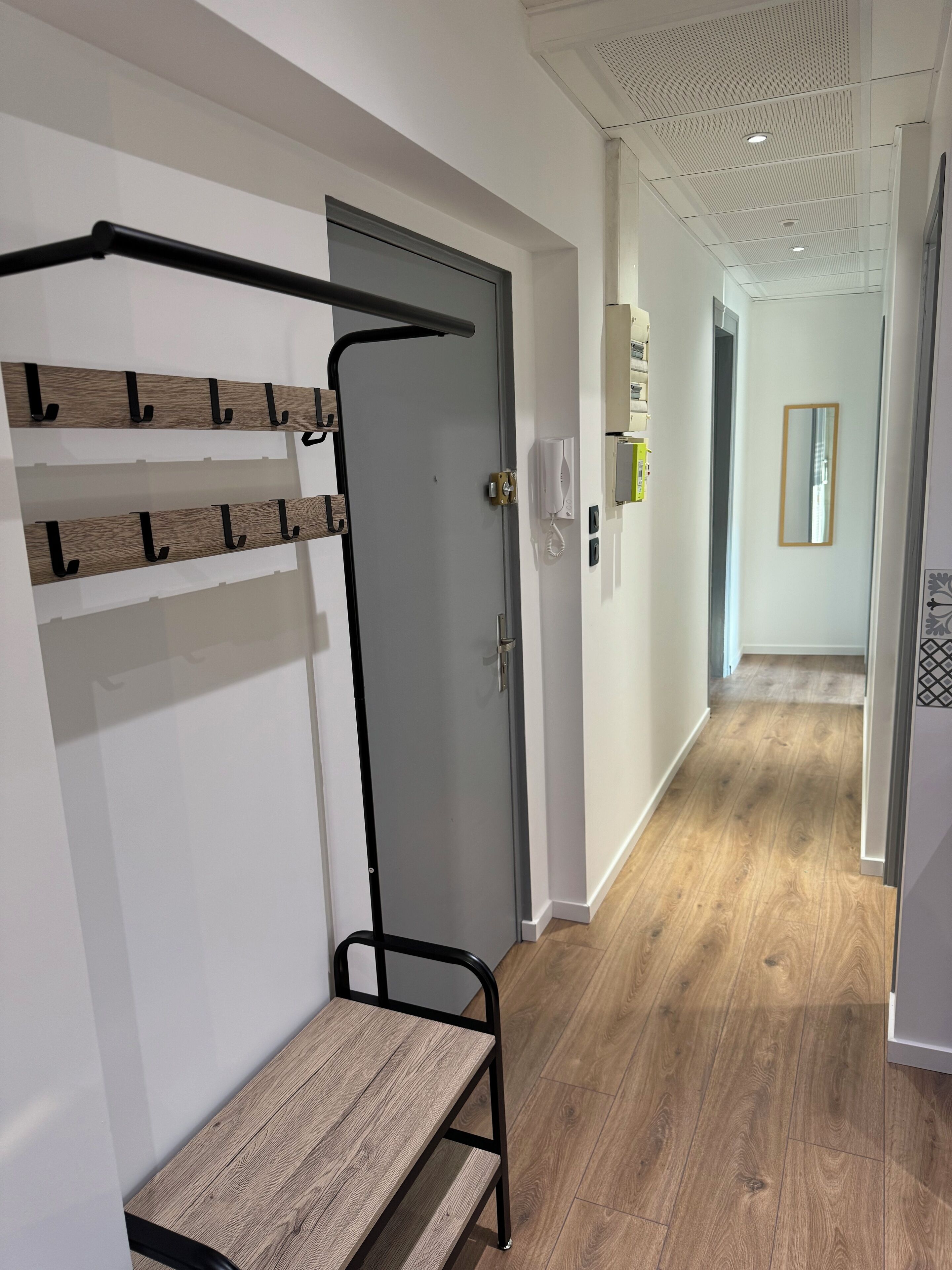 A hallway with a wooden bench, a door with a handle, a wall-mounted telephone, and a mirror.