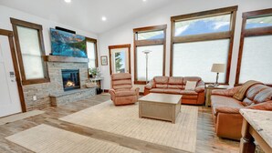 Amplia sala de estar con chimenea de piedra, sofás de cuero y ventanas grandes con vistas al exterior.