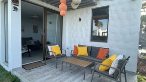 A modern outdoor seating area with a sofa and chairs, a wooden table, and a glass door leading to an interior space. - Apartamerica Garden Apartment, 150 Metres From The (Playa de Las Americas)