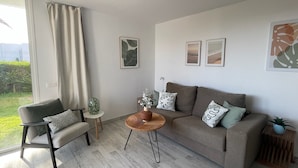 A modern living room with a sofa, armchair, and coffee table, featuring artwork and a view through a large window. - Apartamerica Garden Apartment, 150 Metres From The (Playa de Las Americas)