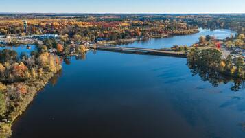 An aerial view of a lake surrounded by autumn-colored trees, a small dock, and a distant water tower.