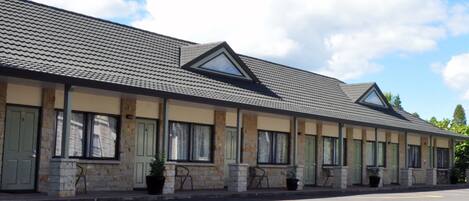 Une rangée de chambres de motel avec un toit plat et de grandes fenêtres, un parking à l’avant et un ciel dégagé.