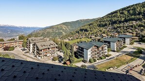 Eine hochgelegene Stadt mit mehrstöckigen Gebäuden, von denen einige Balkone haben, vor einer Bergkulisse.