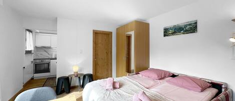 Una habitación pequeña con cama, mesitas de noche, escritorio y kitchenette.